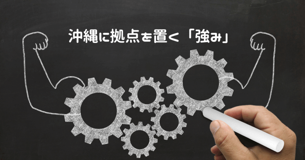 黒板に歯車の両サイドに力瘤のある腕をチョークで書いている手の画像の上真ん中に「沖縄に拠点を置く『強み』」と白い文字がある